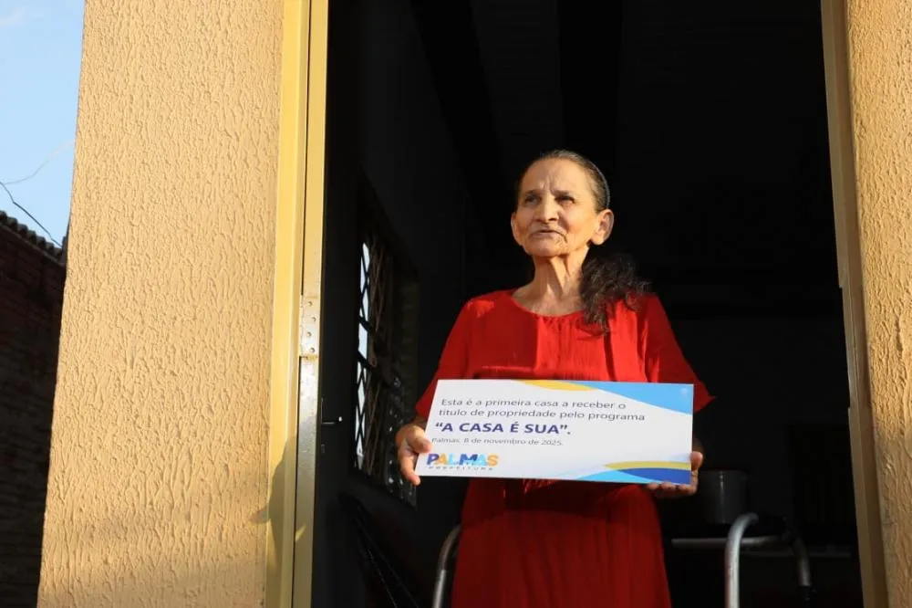 A aposentada Helena Ferreira recebe placa como primeira beneficiária da regularização fundiária da região – Foto: Edu Fortes